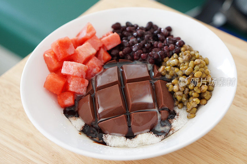 一碗冰镇的巧克力豆腐布丁，上面淋有西瓜、红豆、绿豆和巧克力酱。