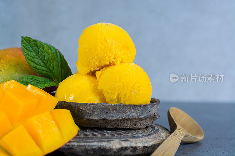 薄荷叶芒果冰沙和芒果水果在黑色的石头碗，灰色纹理的背景