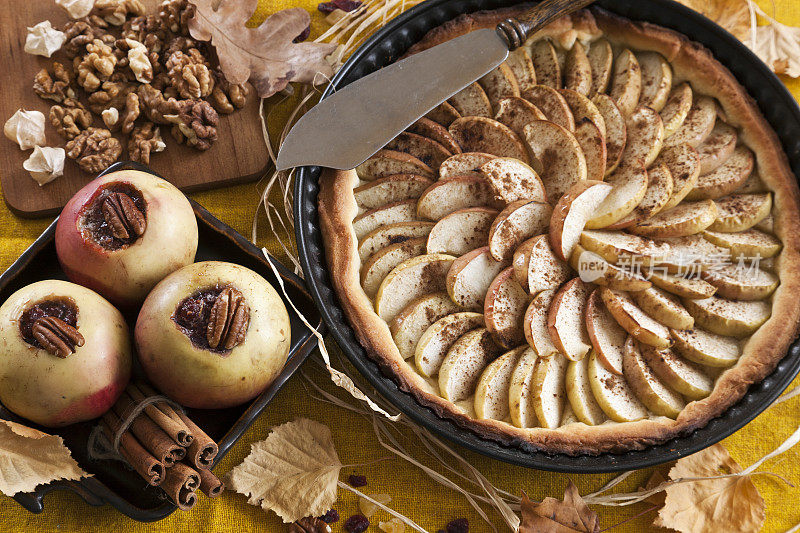 苹果派和苹果烤肉桂和果酱周围的秋叶，在一个古老的木制背景。