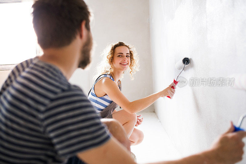 一对年轻夫妇正在粉刷他们新房子的墙壁。
