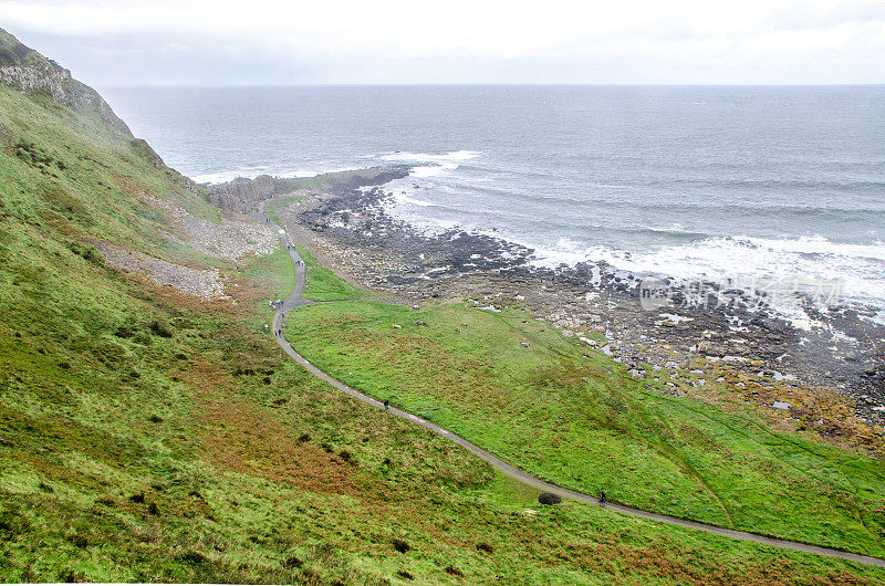 秋天的一天，人们沿着通往北爱尔兰大西洋海岸巨人堤道的小路行走