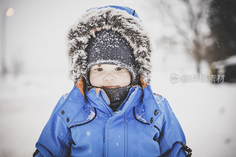 穿着蓝色冬装的小男孩和雪玩