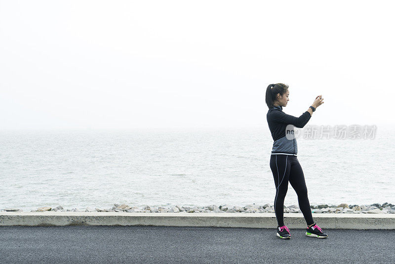 运动女孩在城市海滨用智能手机拍照