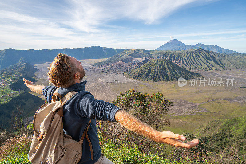 在印度尼西亚，年轻人徒步旅行，手臂伸开站在火山的山顶上，人们旅行的乐趣，冒险的概念，成功和成就