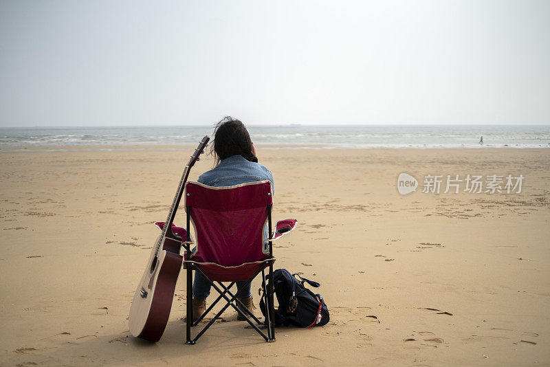 女孩拿着吉他，坐在沙滩户外的椅子上