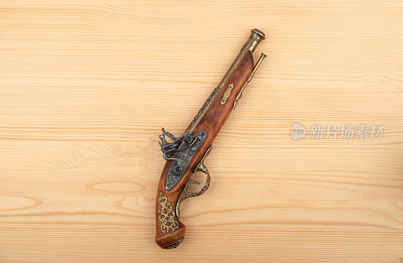 老式的单发枪口装弹手枪，木制背景上有敲击锁。