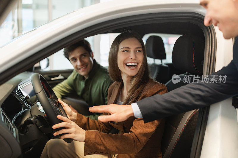 快乐的年轻夫妇试驾新车，推销员帮助他们在汽车经销商做出最佳选择