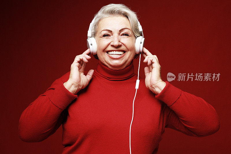 生活方式、情感与老年人观念:老妇人穿着红色毛衣，戴着耳机听音乐