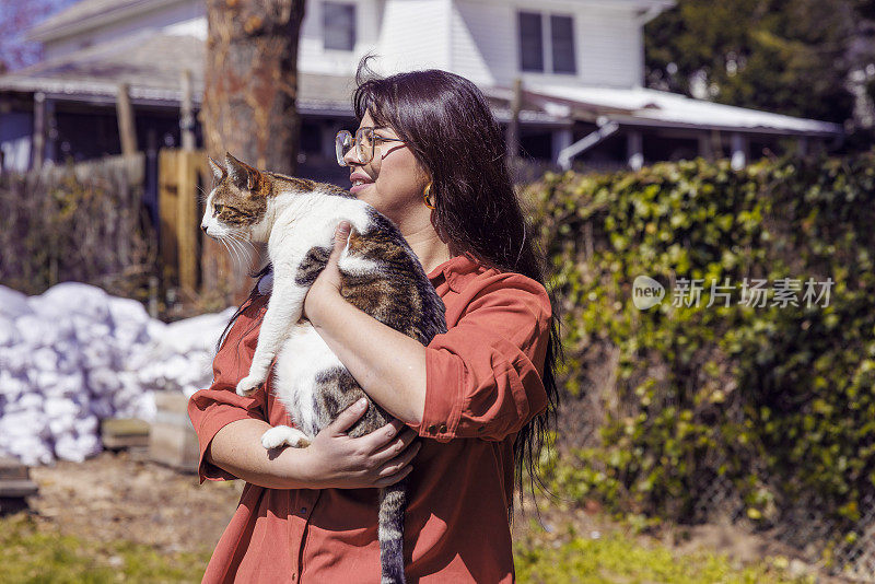 春天的一个阳光明媚的日子里，一位年轻的拉丁女子和一只猫在户外散步。