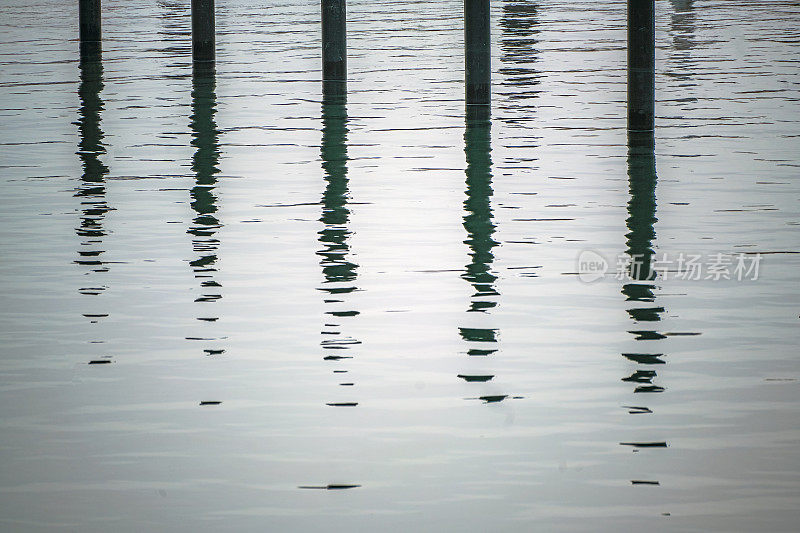 黑色的系泊桩或海豚在水中的倒影，在一个灰色的11月的一天，在波罗的海的空游艇码头，抽象的图像，几乎单色，复制空间
