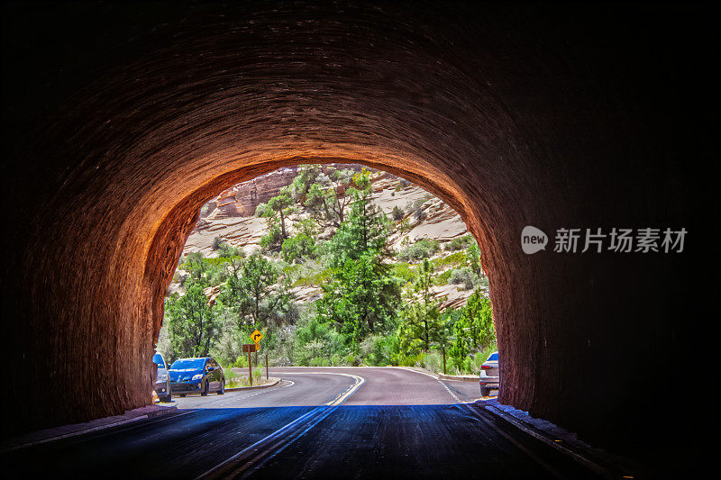 锡安国家公园南端隧道尽头的灯光显示出明亮的灯光、树木、悬崖和几辆停着的汽车