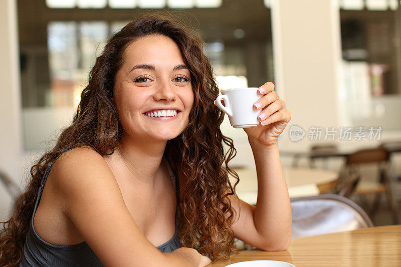 快乐的女人拿着咖啡杯在酒吧里看着你