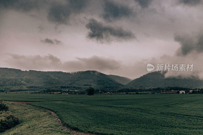 风暴景观，田野和树木的旅行摄影。蓝天白云，绿草如茵。为，雾霾画面的山和小山。恶劣天气下的山谷照片。