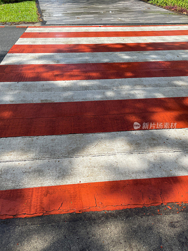 红白条纹斑马线在柏油路上的特写图像，阳光和阴影斑驳，高架视图，重点在前景