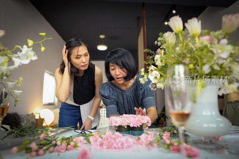 一位亚洲美丽的花艺女老师目前正在教花艺学生如何安排花艺材料，创造美丽的花艺作品。