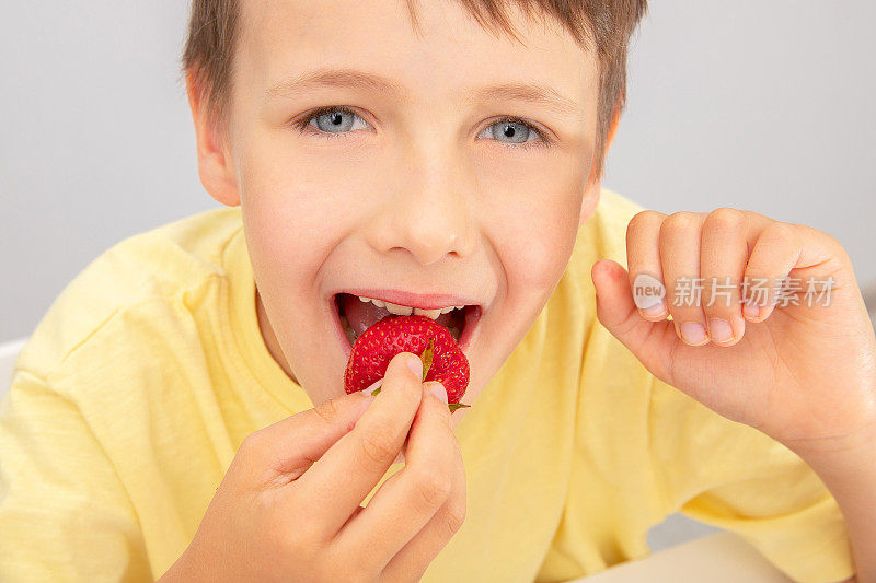 孩子手里拿着一个草莓，张开嘴吃浆果。健康饮食的概念