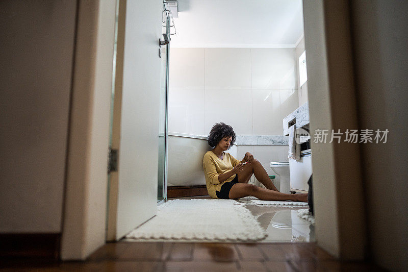 悲伤的年轻女子拿着验孕棒坐在家里浴室的地上