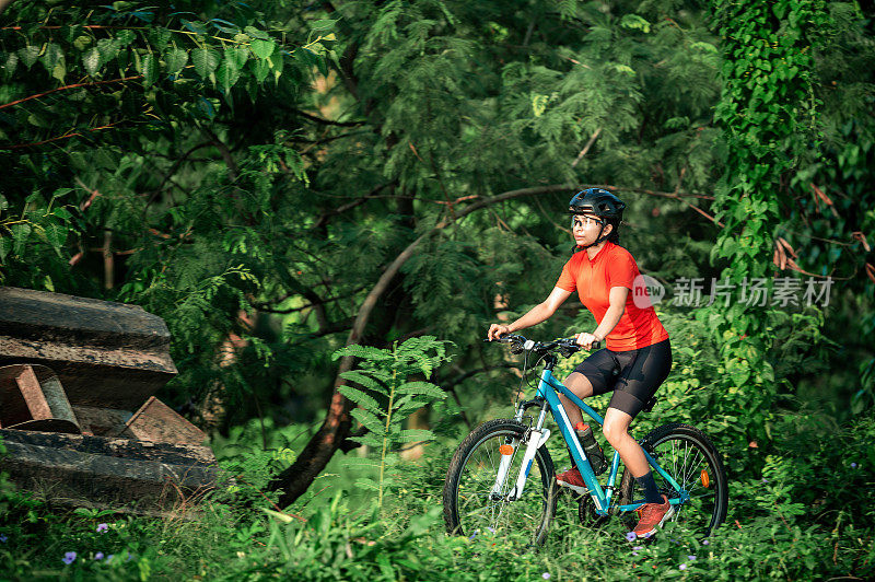 年轻的女子骑着她的山地车在夏日的森林小径上享受美丽的骑行