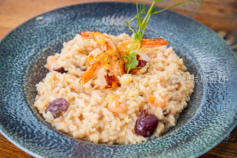 餐厅餐桌上盘子里的意大利烩饭配大虾和黑橄榄的特写