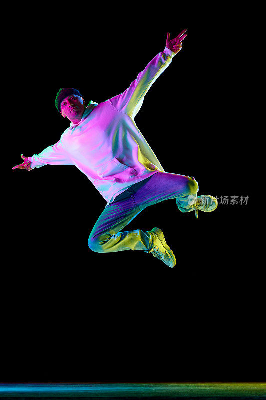 年轻的男舞者，运动的家伙，在霓虹灯的黑色背景下，穿着时尚的衣服，自由地跳舞，嘻哈的动作。