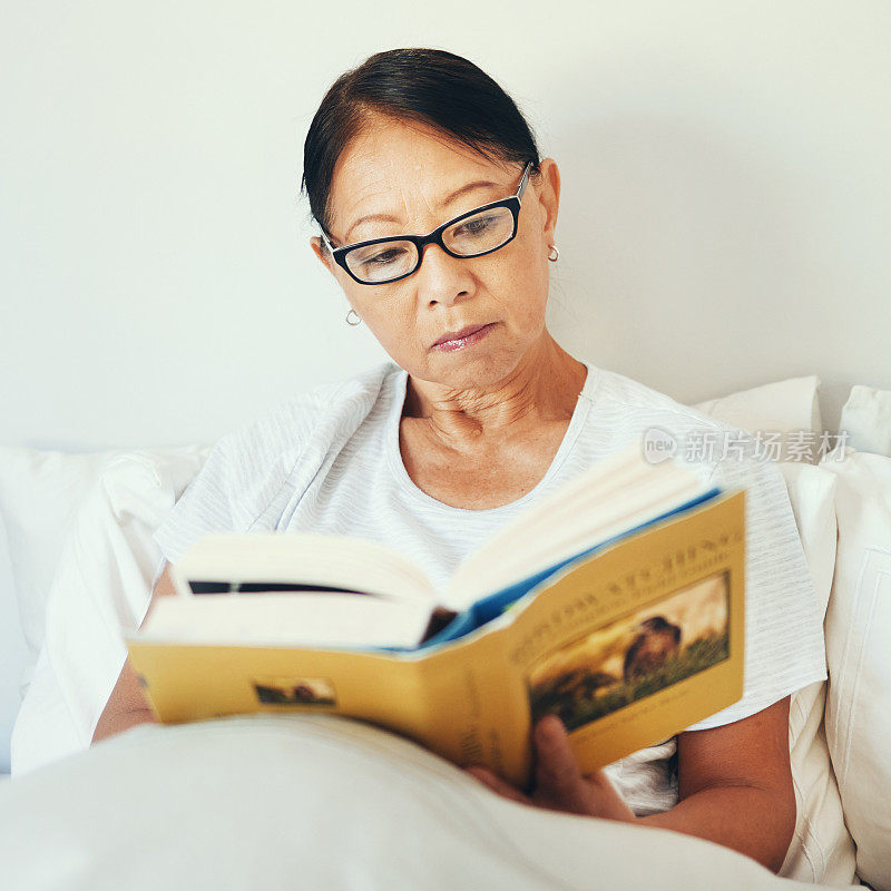 成熟的女人在卧室看书是为了故事，在家里看书是为了小说和知识。严肃的亚洲人，戴着眼镜，舒舒服服地躺在床上，用文学来休息，用爱好和放松来享受休息