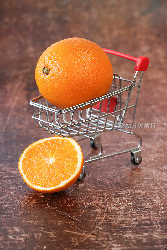 整个橙子的微缩特写图像，模型购物车，健康食品店，棕色背景上的半水果，重点在前景，健康饮食理念