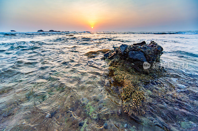 日落在海浪与岩石前景，清澈的水，和遥远的地平线，Hikkaduwa。