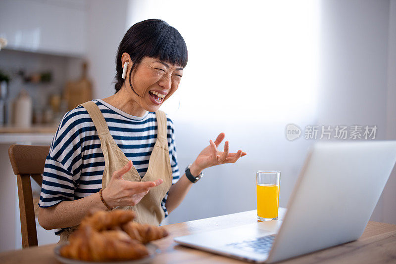 一个亚洲女人一边用笔记本电脑打字一边吃早餐