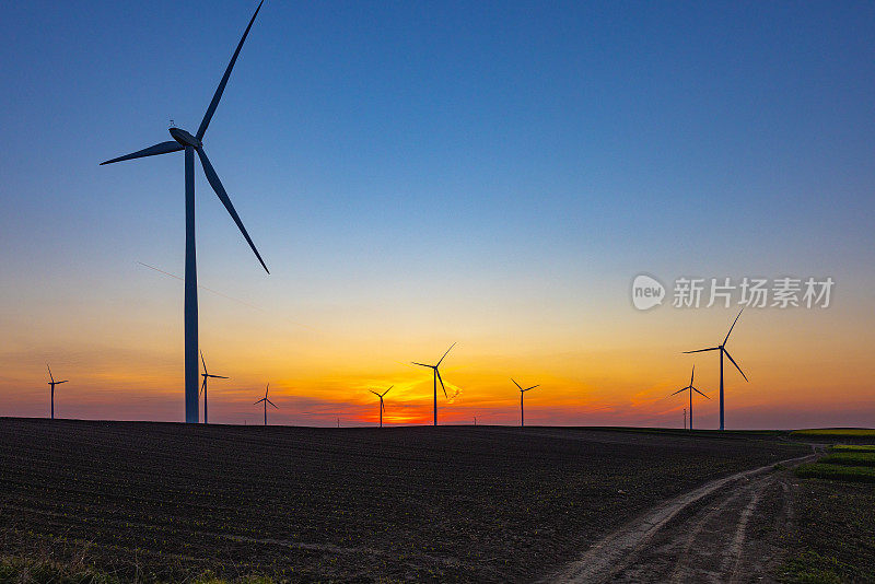 美丽的夕阳下，土路旁农田上的风力涡轮机