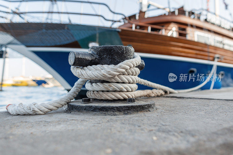 漂亮昂贵的游艇用一根绳子拴在港口的金属系柱上。一艘海船停在码头上。电缆和金属锚的特写。保险的概念。海上旅行