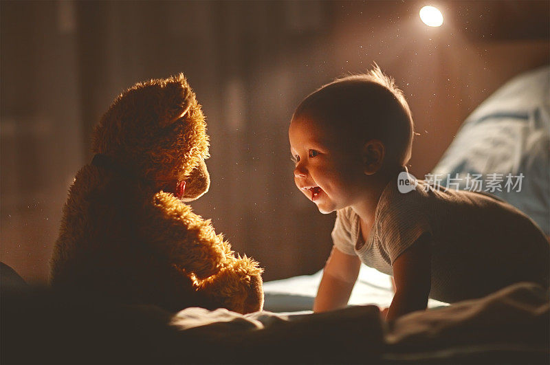 快乐的宝宝和泰迪熊在床上笑