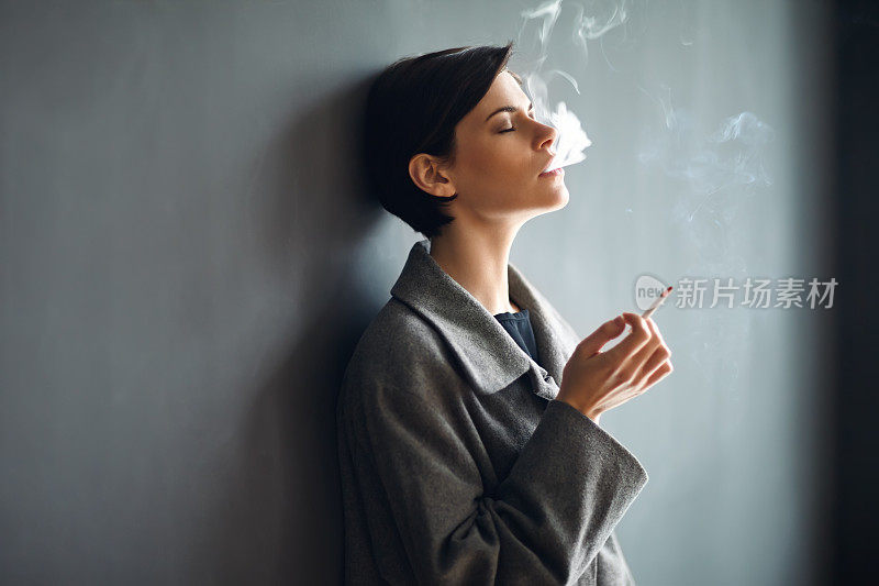 在黑暗的背景上吸烟的时尚女人的肖像