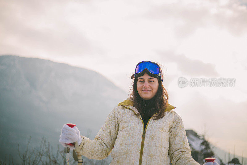 近景美丽的年轻女子在冬天的衣服站在一边，手拿木棍的背景雪山