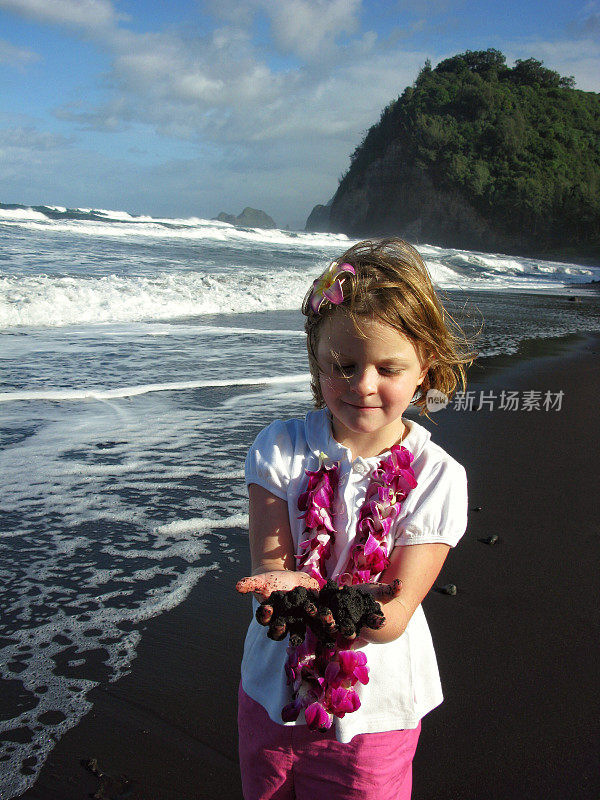 蕾项链戴着女孩的孩子拿着黑色的沙子，夏威夷海滩