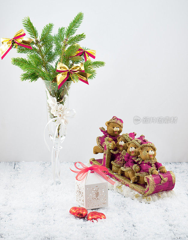白色装饰的圣诞树，白色的礼盒，粉色和金色的玩具熊在雪橇上，糖果和雪在复古复古的白色桌子上在白色的背景