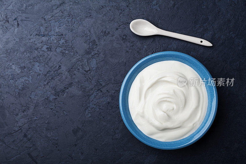 希腊酸奶在蓝色的碗在黑色的桌子俯视图。为文本复制空间。