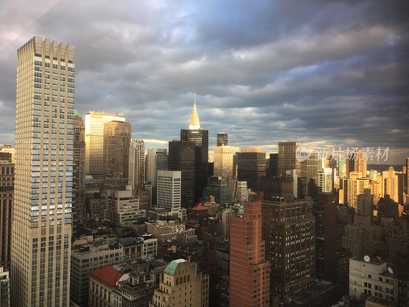 云层散开，阳光洒落在曼哈顿中城，摩天大楼在阳光下闪闪发光。从摩天大楼办公室的窗户拍摄到的纽约市上空的暴风云。望着窗口。