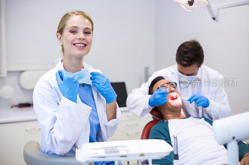 微笑的牙医站在她的同事检查病人的背景肖像