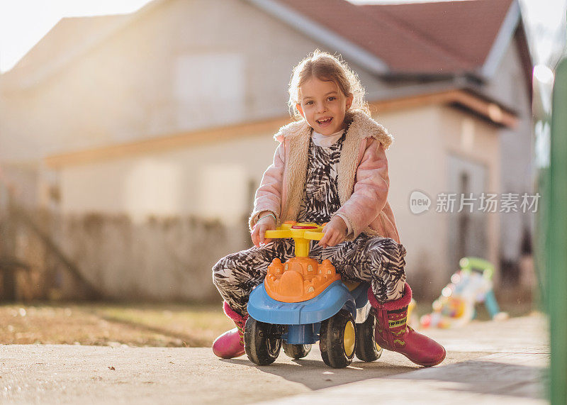 快乐的小女孩开着玩具车在户外看相机。