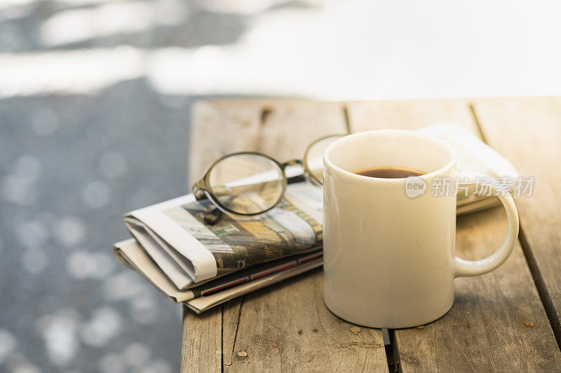 早上，在花园里的木桌上放着一杯热咖啡、老花镜和报纸