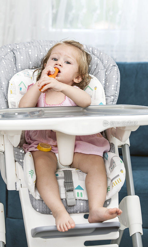 快乐的小女孩在高椅子上吃胡萝卜。