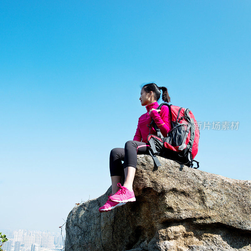 女背包客坐在山顶的岩石上