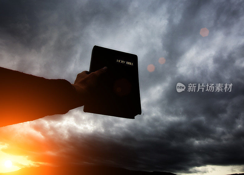 手拿着圣经向着灰色的云朵
