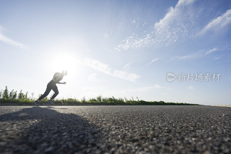 年轻的男运动员在柏油路上迎着天空奔跑