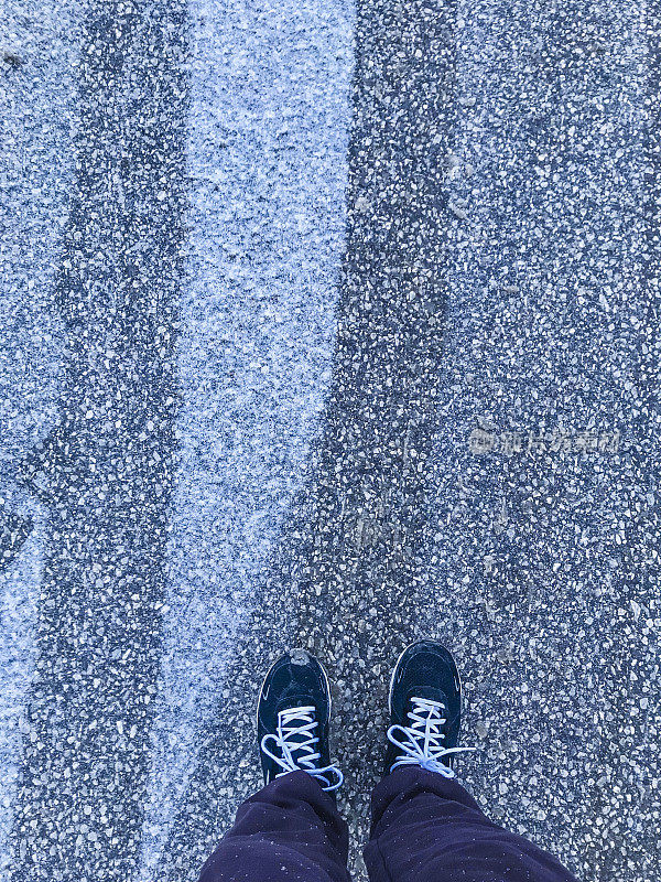 穿着跑步鞋的脚在寒冷的冬天的人行道上行走