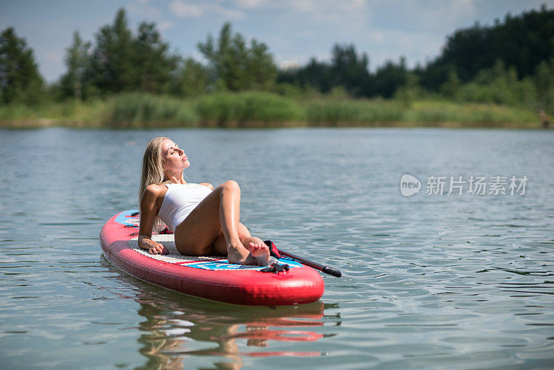 年轻的女孩正在她的站立式桨板上晒日光浴