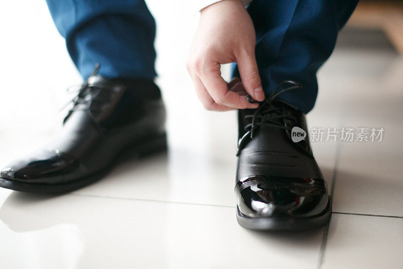 新郎正在系着一只黑皮鞋的鞋带