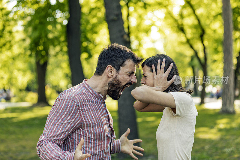 一对年轻夫妇在公园里吵架。年轻夫妇有一个夏天的一天争吵。站在公园外面，困惑的年轻女子打着手势，看着她的男朋友