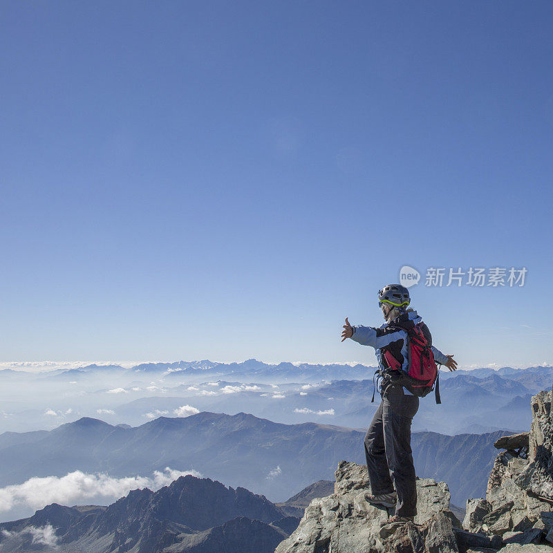 女攀登者双手伸出站在山顶