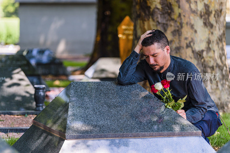 悲伤中的男性鳏夫与玫瑰花束在墓地